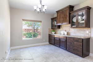 Kitchen featuring light stone countertops, hanging light fixtures, a notable chandelier, decorative backsplash, and dark brown cabinets