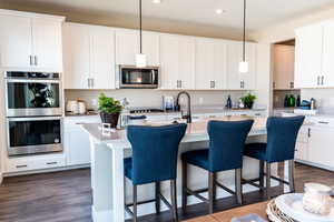 Kitchen featuring dark hardwood / wood-style floors, hanging light fixtures, an island with sink, white cabinets, and appliances with stainless steel finishes