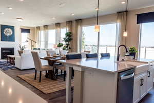 Kitchen featuring a large fireplace, a kitchen island with sink, hanging light fixtures, white cabinets, and sink