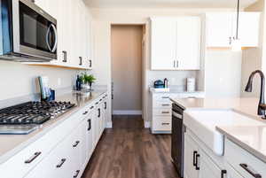 Kitchen featuring sink, appliances with stainless steel finishes, white cabinets, hanging light fixtures, and dark wood-type flooring