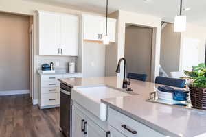 Kitchen featuring stainless steel dishwasher, dark hardwood / wood-style floors, decorative light fixtures, white cabinets, and sink