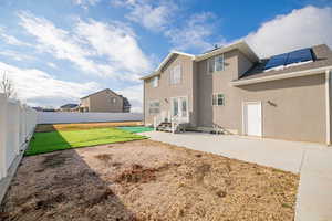 Rear view of property featuring a patio, a yard, and solar panels