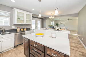 Kitchen featuring white cabinets, hanging light fixtures, sink, stainless steel dishwasher, and ceiling fan with notable chandelier