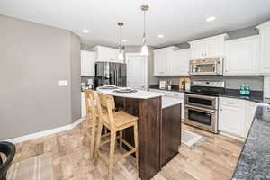 Kitchen with appliances with stainless steel finishes, hanging light fixtures, light wood-type flooring, a kitchen island, and white cabinetry