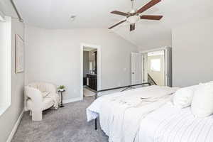 Carpeted bedroom featuring lofted ceiling, ensuite bathroom, and ceiling fan