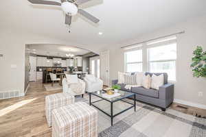 Living room featuring ceiling fan with notable chandelier and light wood-type flooring