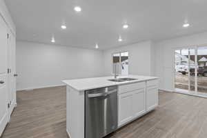 Kitchen featuring white cabinets, laminate flooring, an island with sink, sink, and stainless steel dishwasher