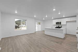 Kitchen with a center island with sink, appliances with stainless steel finishes, white cabinets, laminate flooring, and sink