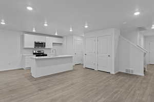 Kitchen featuring sink, white cabinetry, laminate flooring, a center island with sink, and appliances with stainless steel finishes