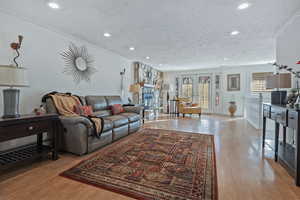 Living room featuring light wood-type flooring, a fireplace, a textured ceiling, and ornamental molding