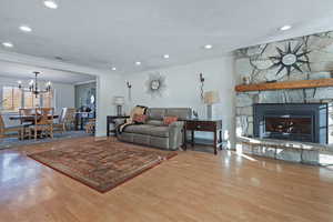 Living room with a stone fireplace, a chandelier, wood-type flooring, ornamental molding, and a textured ceiling