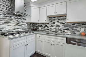 Kitchen with tasteful backsplash, white cabinetry, and wall chimney exhaust hood