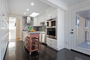 Kitchen featuring stainless steel appliances, wall chimney range hood, tasteful backsplash, crown molding, and white cabinets