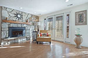 Living area with hardwood / wood-style flooring, french doors, ornamental molding, and a stone fireplace