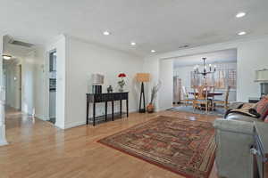 Living room with a textured ceiling, light wood-type flooring, an inviting chandelier, and crown molding