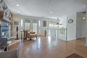 Living area featuring french doors, a textured ceiling, ceiling fan, and a stone fireplace