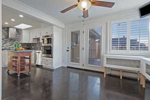 Kitchen featuring stainless steel appliances, white cabinetry, crown molding, and wall chimney range hood