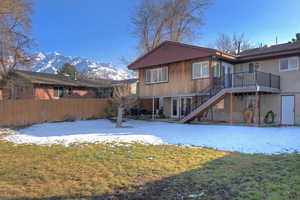 Snow covered back of property featuring a deck with mountain view and a yard