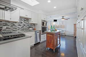 Kitchen featuring wall chimney exhaust hood, white cabinetry, appliances with stainless steel finishes, ceiling fan, and sink