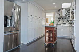 Kitchen with white cabinetry, wall chimney exhaust hood, decorative backsplash, a skylight, and stainless steel fridge with ice dispenser