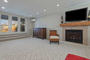 Living area with a tile fireplace, a wall unit AC, ornamental molding, and light carpet