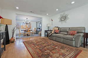 Living room featuring a notable chandelier, crown molding, and wood-type flooring