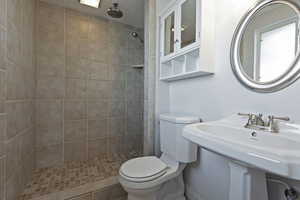 Bathroom with toilet, a tile shower, and sink