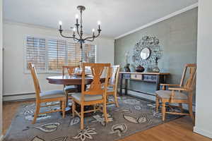 Dining area with a baseboard heating unit, an inviting chandelier, crown molding, and wood-type flooring