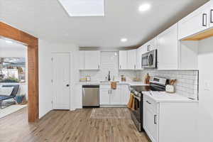 Kitchen featuring sink, white cabinetry, backsplash, and appliances with stainless steel finishes