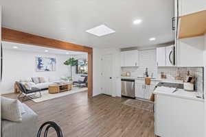 Kitchen featuring stainless steel appliances, light hardwood / wood-style floors, backsplash, white cabinetry, and sink