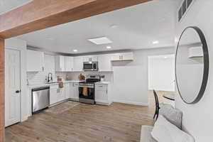 Kitchen featuring light hardwood / wood-style floors, stainless steel appliances, sink, white cabinetry, and tasteful backsplash