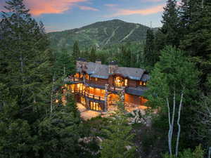 Back of house at dusk featuring a view of trees, a mountain view, stone siding, a balcony, and log siding
