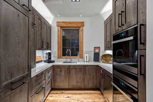 Kitchen with sink, light hardwood / wood-style floors, wall oven, and black dishwasher