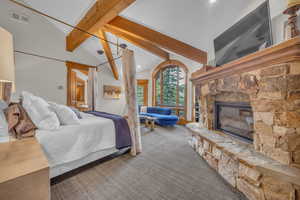 Carpeted bedroom with beam ceiling, a stone fireplace, and high vaulted ceiling
