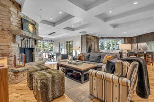 Living area with light wood-type flooring, recessed lighting, coffered ceiling, a stone fireplace, and beam ceiling