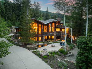 Back of property at dusk with a patio, a chimney, stairway, stone siding, and a balcony