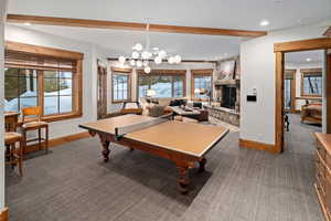 Recreation room featuring a fireplace, an inviting chandelier, dark carpet, and plenty of natural light