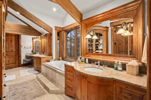 Bathroom featuring vanity, tiled tub, and vaulted ceiling with beams