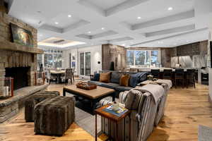 Living room with coffered ceiling, beamed ceiling, light hardwood / wood-style flooring, and a stone fireplace