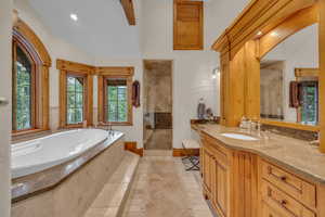 Bathroom with tiled shower, a garden tub, vanity, inlaid floor details, and lofted ceiling