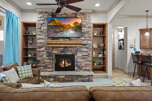 Living room featuring ceiling fan, built in features, crown molding, and a fireplace