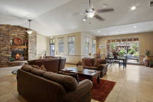 Living room featuring ceiling fan, a stone fireplace, and lofted ceiling