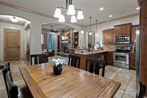 Dining space with built in shelves, crown molding, ceiling fan with notable chandelier, a fireplace, and sink