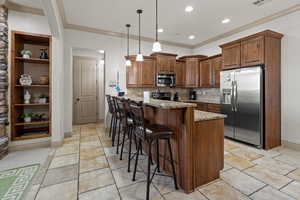 Kitchen with light stone counters, decorative light fixtures, stainless steel appliances, crown molding, and a kitchen breakfast bar