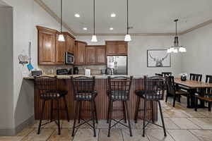 Kitchen with kitchen peninsula, light stone countertops, tasteful backsplash, appliances with stainless steel finishes, and ornamental molding