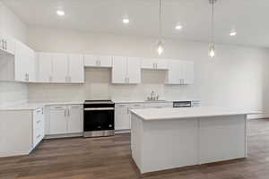 Kitchen with appliances with stainless steel finishes, dark hardwood / wood-style floors, sink, white cabinetry, and decorative light fixtures