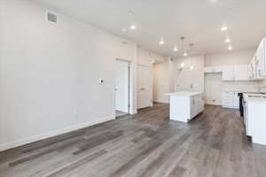 Kitchen with sink, decorative light fixtures, white cabinets, hardwood / wood-style floors, and a kitchen island