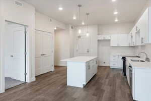 Kitchen with pendant lighting, dark wood-type flooring, a kitchen island, sink, and white cabinetry