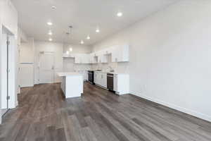 Kitchen featuring white cabinets, stainless steel appliances, a center island, pendant lighting, and sink