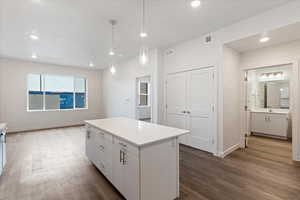 Kitchen featuring dark wood-type flooring, hanging light fixtures, a center island, white cabinets, and sink